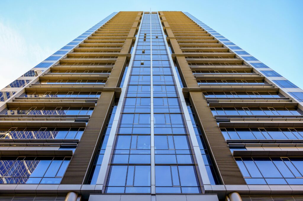 Low angle view of a modern skyscraper with glass façade, reflecting clear blue sky.